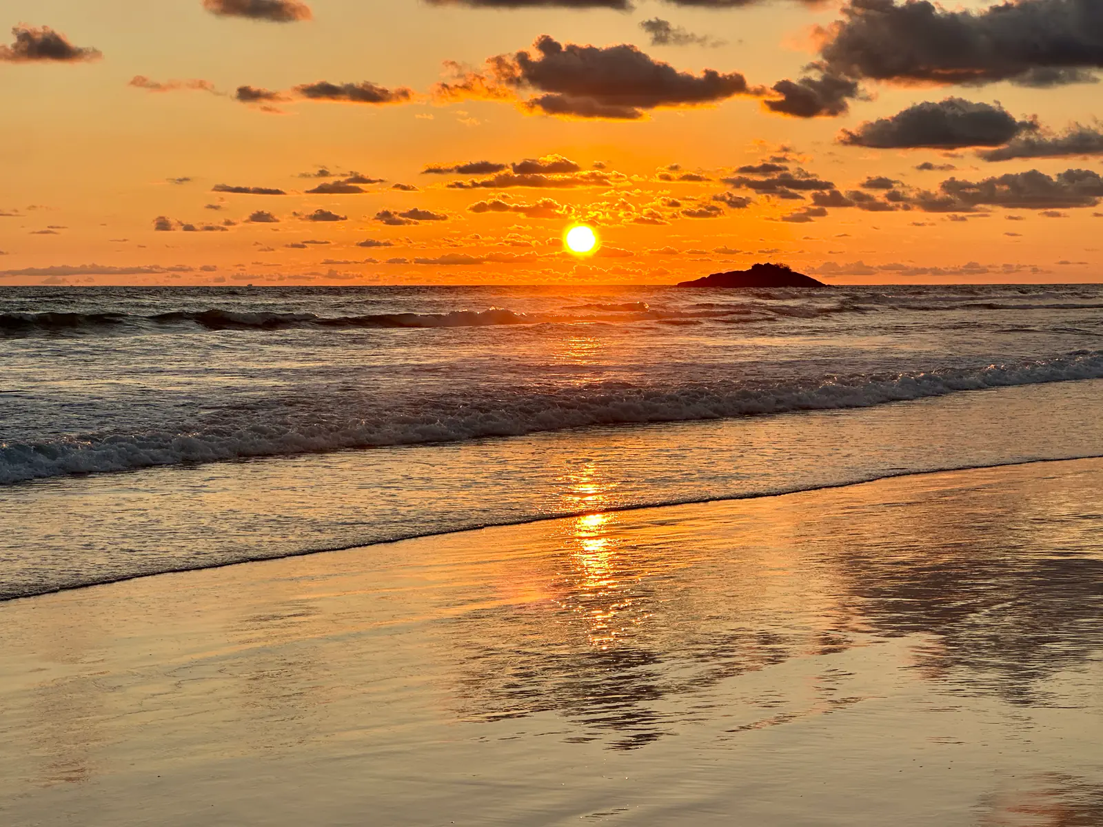 Sonnenuntergang über dem Meer, davor eine kleine Felsinsel